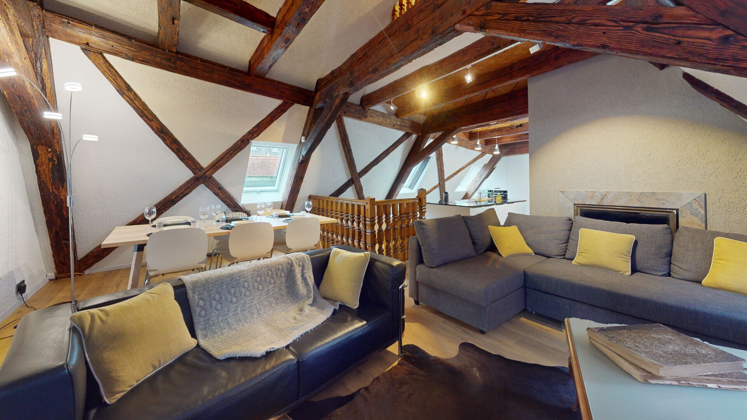 Une pièce confortable de style loft, avec des poutres apparentes, un coin repas comprenant une table et des chaises, et un espace détente avec un canapé et des fauteuils.