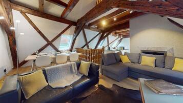 Une pièce confortable de style loft, avec des poutres apparentes, un coin repas comprenant une table et des chaises, et un espace détente avec un canapé et des fauteuils.
