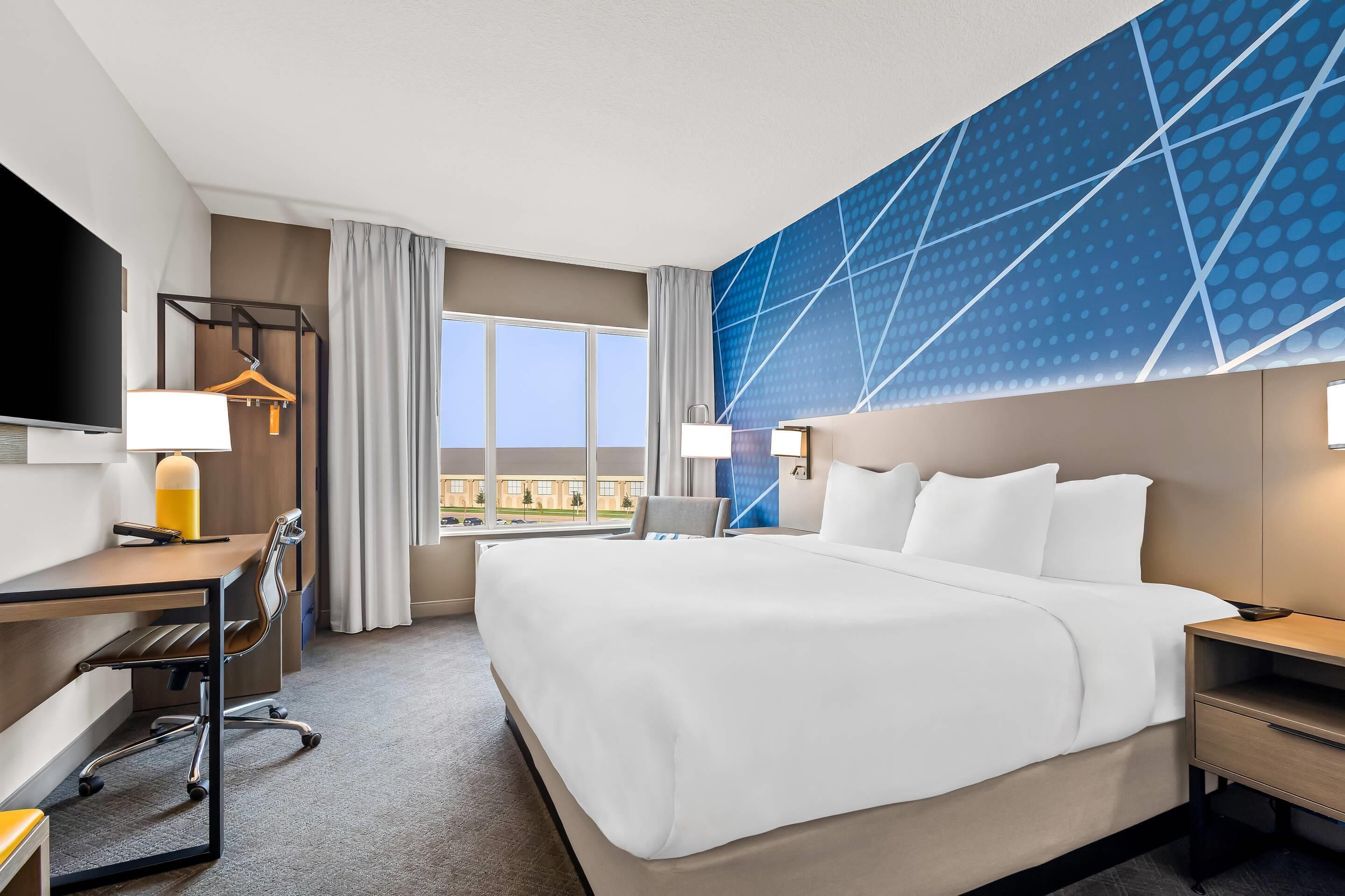 A hotel room with a large bed, a desk with a chair, a TV, and a window with curtains.