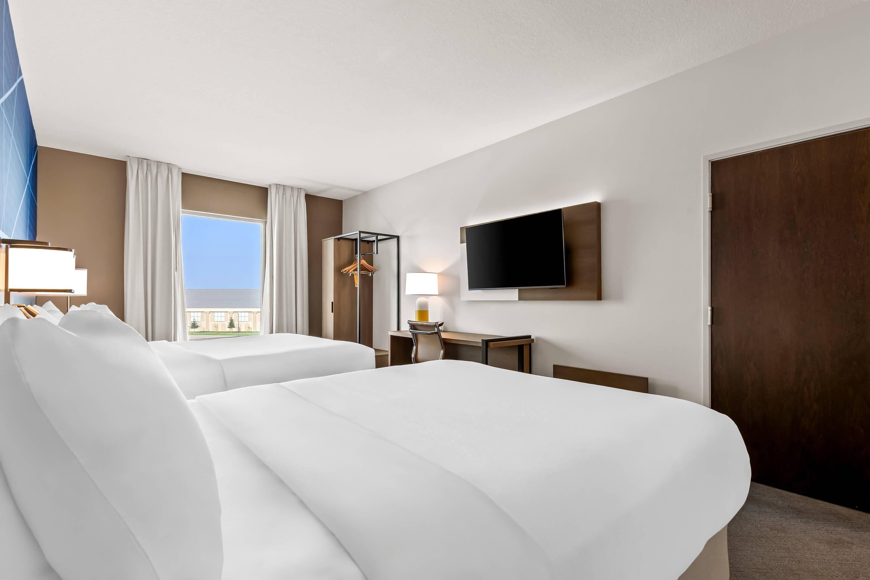 Habitación de hotel con dos camas, un escritorio, una silla, un televisor y una ventana con cortinas.
