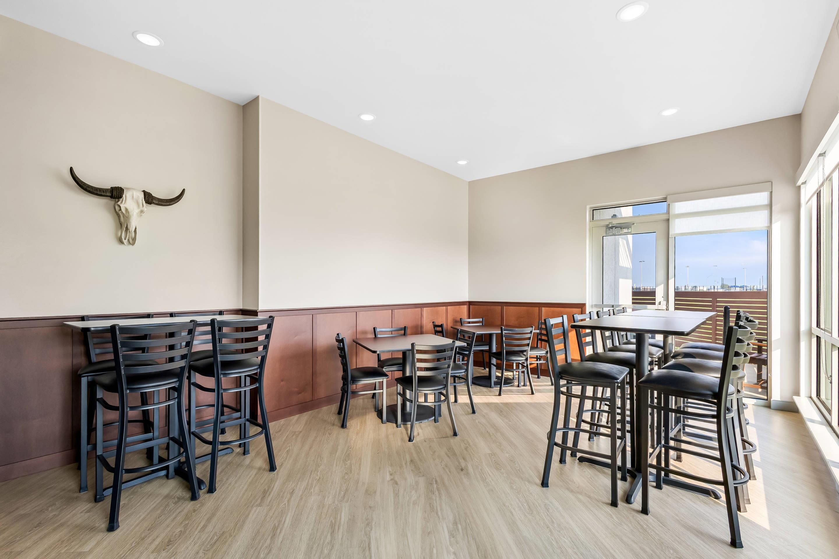 A restaurant with high tables and chairs, a bull skull decoration on the wall, and large windows offering a view.