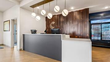 Zona de recepción con diseño moderno, que incluye un mostrador, una computadora y un refrigerador con bebidas.