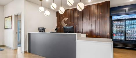 A reception area with a modern design, featuring a counter, a computer, and a refrigerator stocked with beverages.