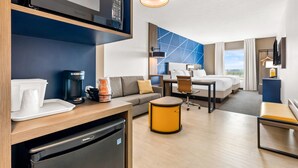 A modern hotel room with a kitchenette, a sofa, a dining table, a small round table, a bed, and a view of the outdoors. - Comfort Inn & Suites at Sanford Sports Complex (Sioux Falls)