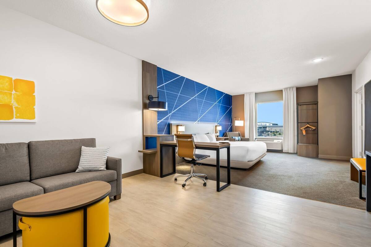 A modern hotel room with a sofa, a desk, a bed, and a view of the city.