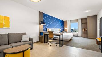 A modern hotel room with a sofa, a desk, a bed, and a view of the city.