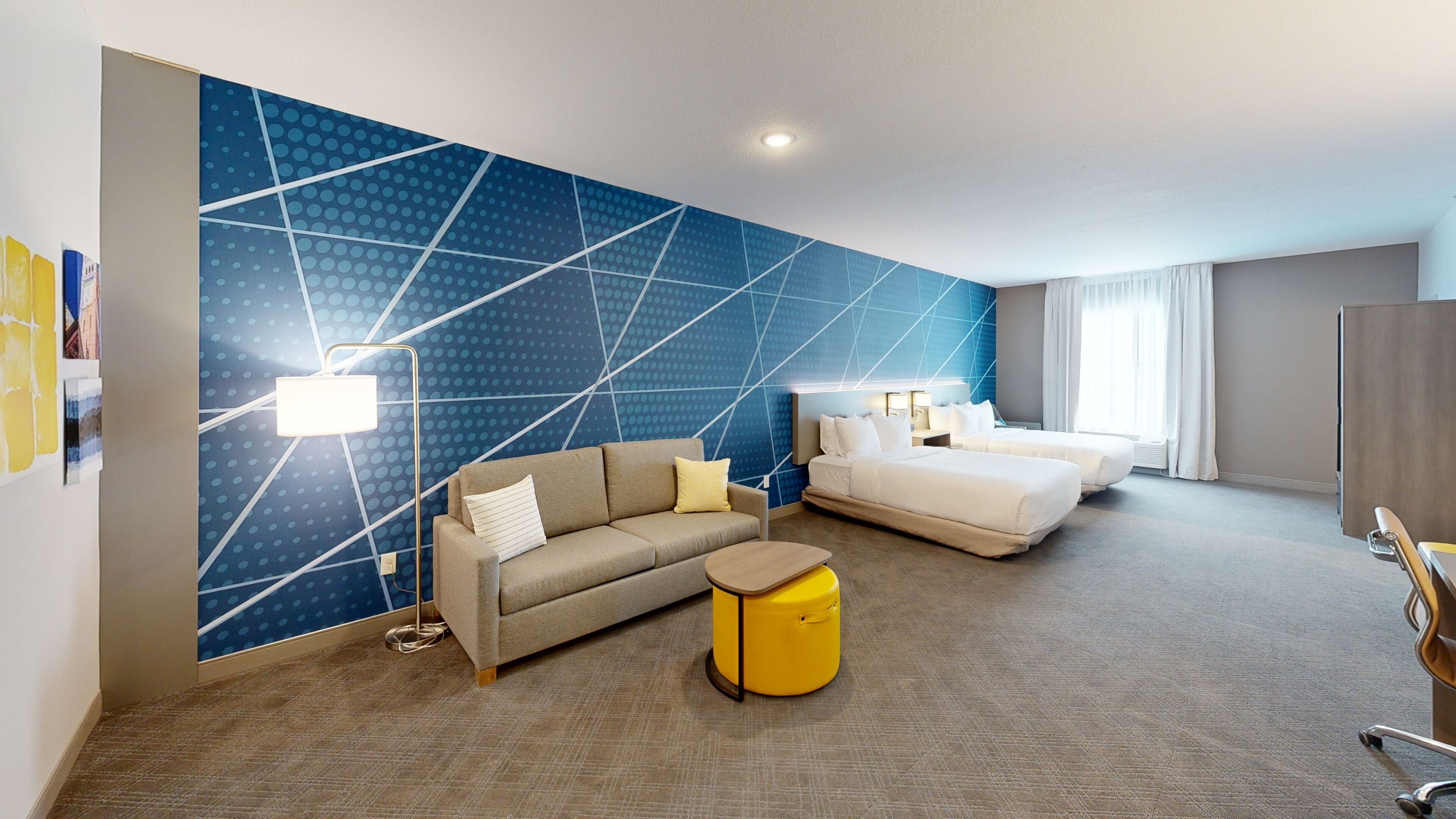 A hotel room with a sofa, a bed, a small round table, and a wall with a geometric pattern.