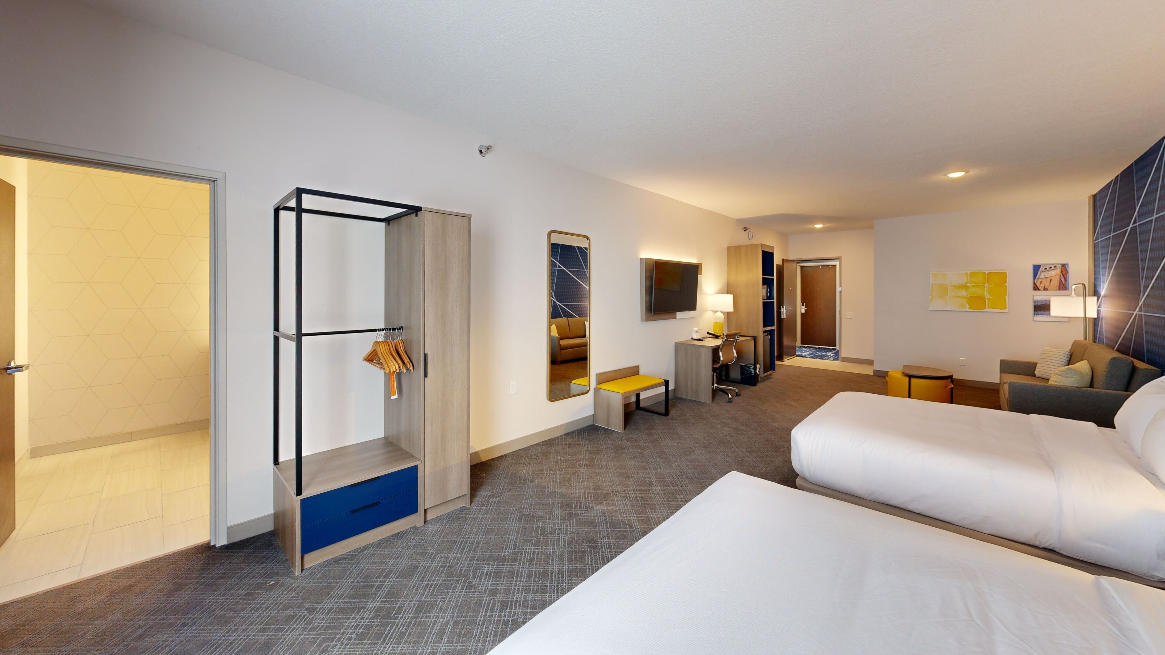 A hotel room with a bed, a desk, a chair, a wardrobe, and a mirror.