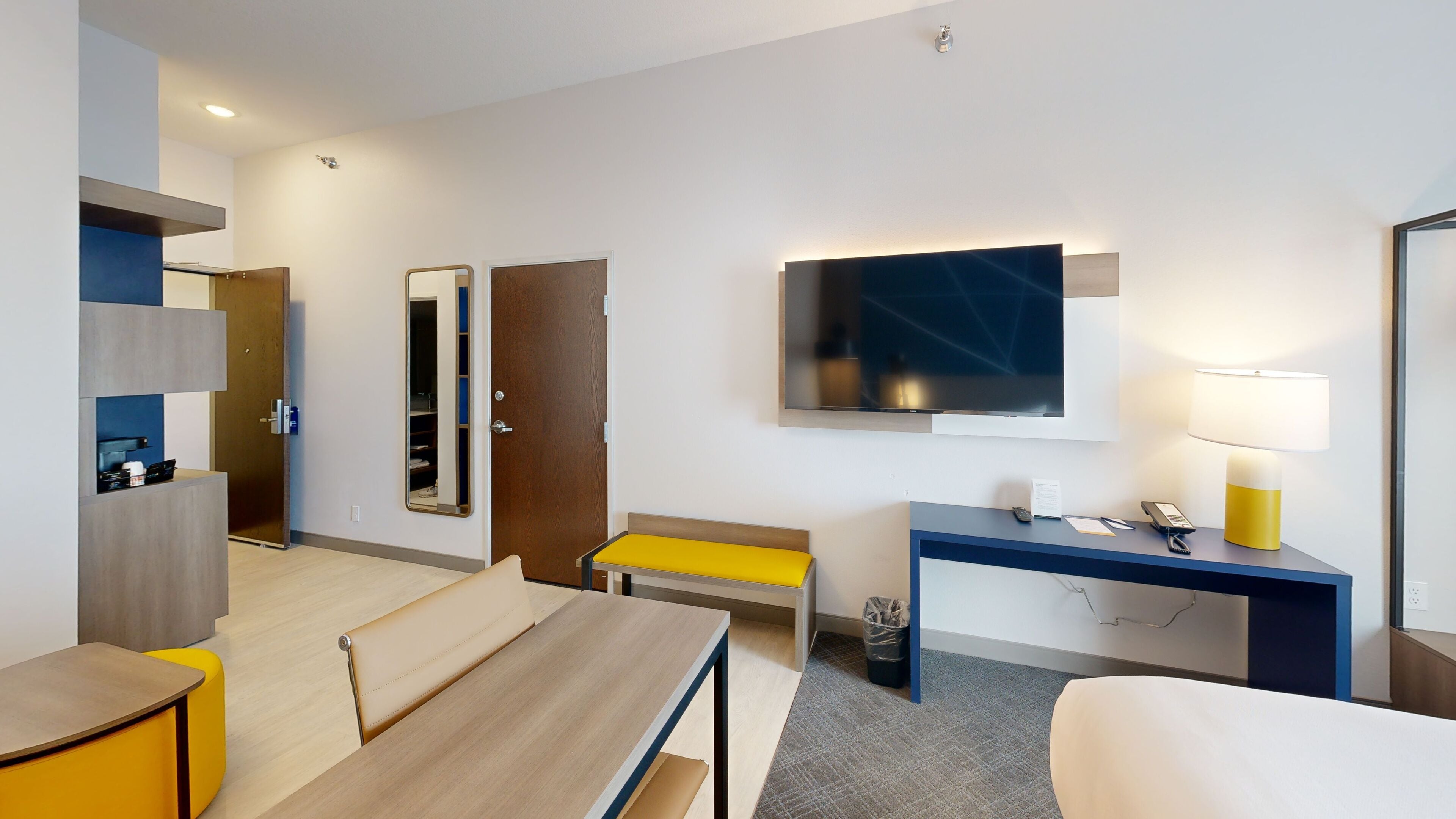 Habitación de hotel moderna con cama, escritorio, silla, televisor y una mesita.