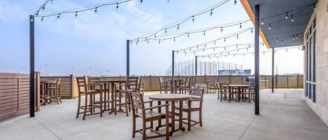 An outdoor patio area with tables and chairs, string lights, and a view of the city skyline.