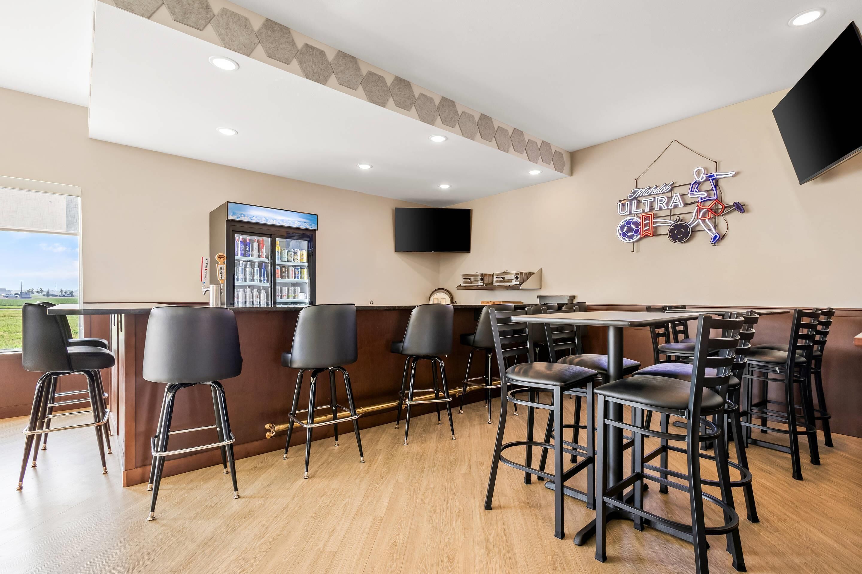 A bar area with stools, a television, a neon sign, and a refrigerator.