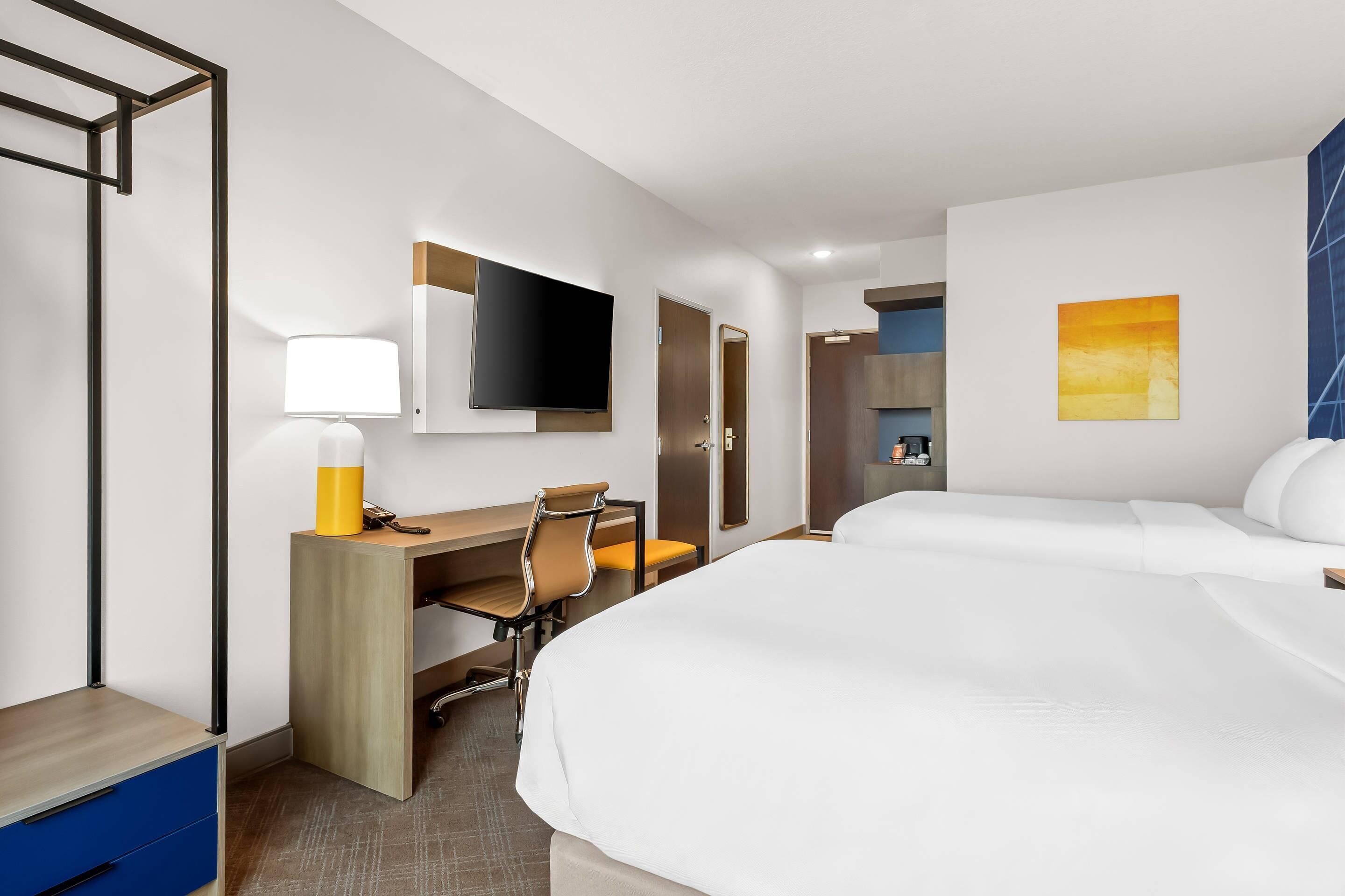 Una habitación de hotel con cama, escritorio con silla, televisor y un cuadro en la pared.