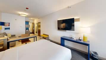 A hotel room with a large bed, a desk with a lamp, a television, and a seating area with a sofa and chairs.