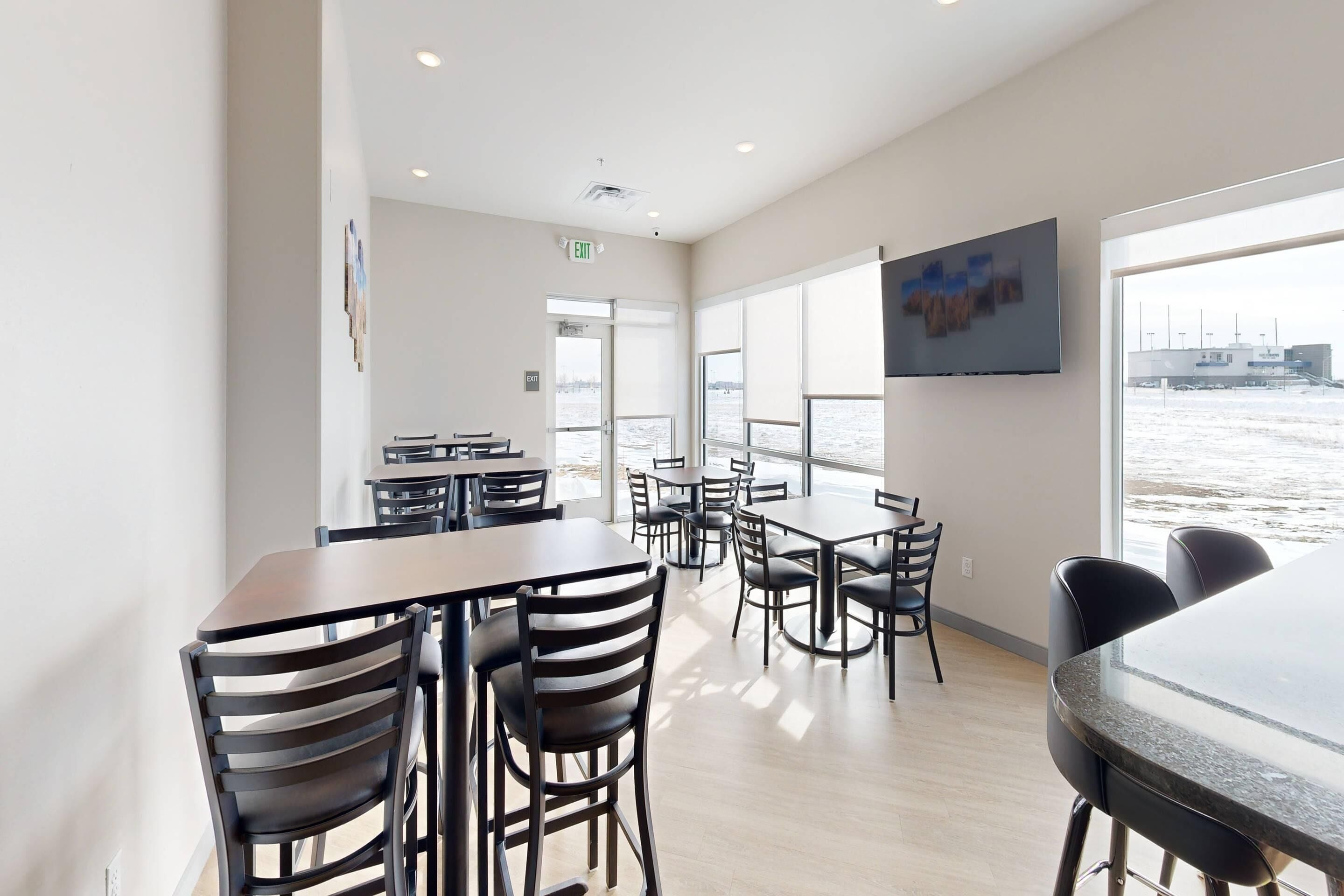 Un comedor moderno con mesas y sillas, ventanas amplias y vista al agua.