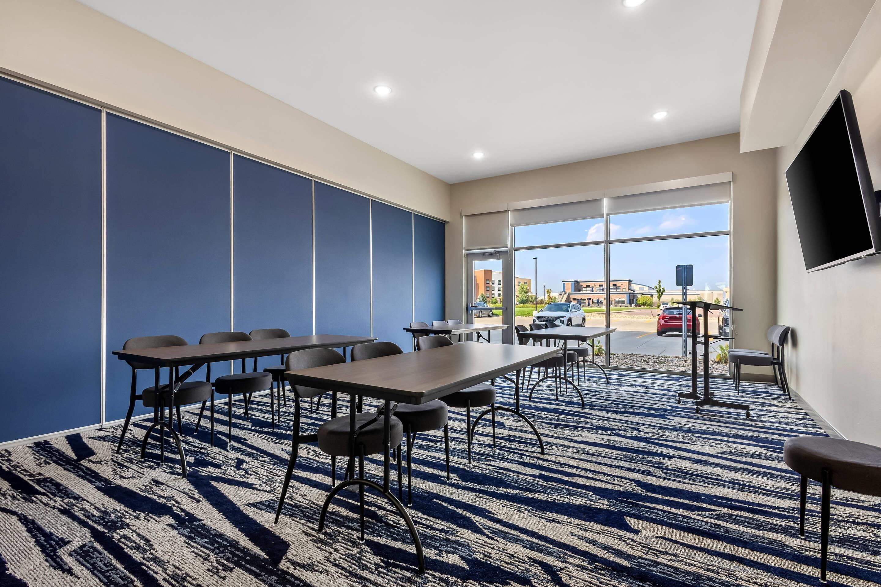 A conference room with tables and chairs, large windows, and a flat-screen TV.