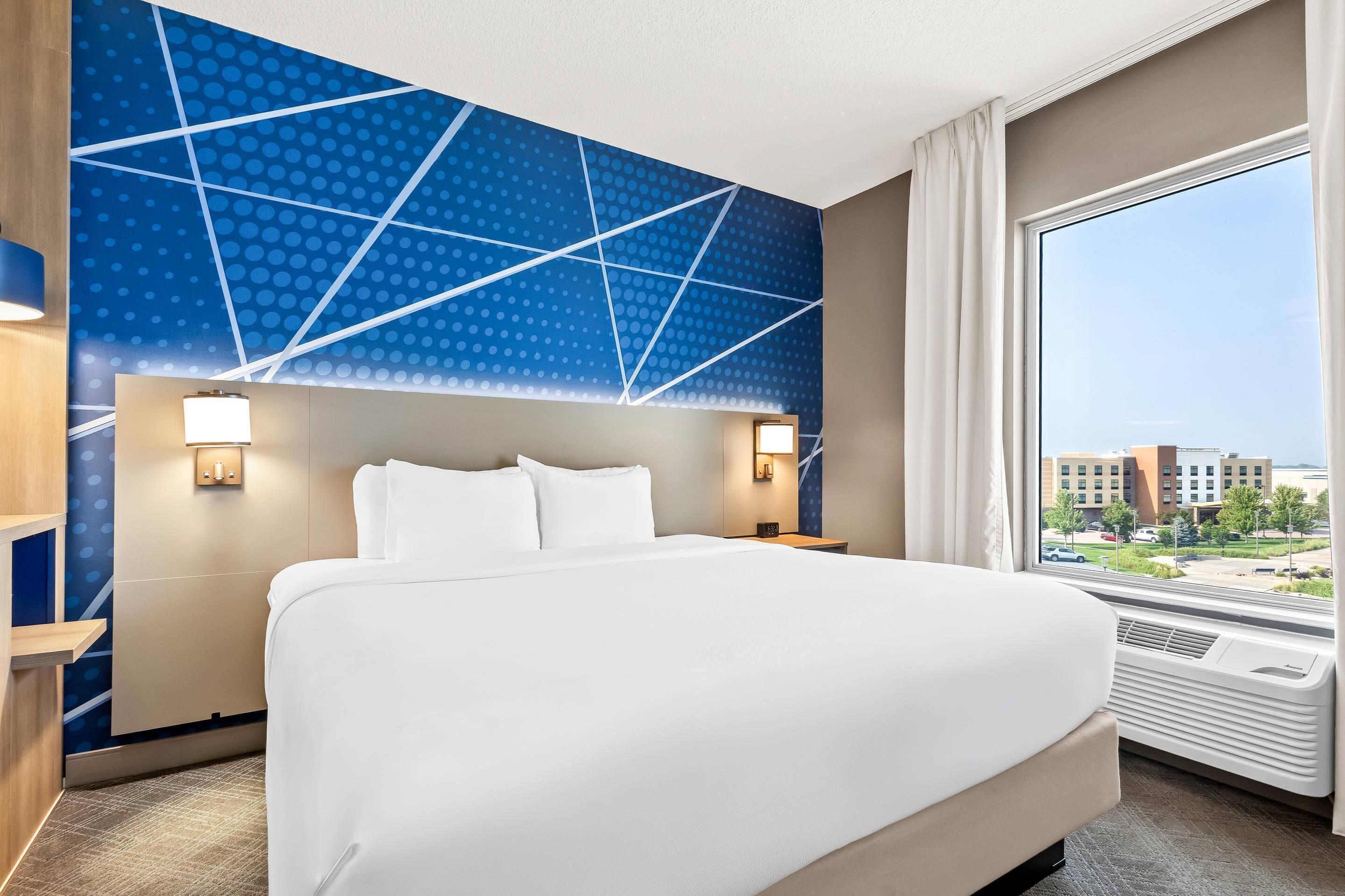 Habitación de hotel con una cama grande, vista de la ciudad a través de una ventana y pared con diseño azul.