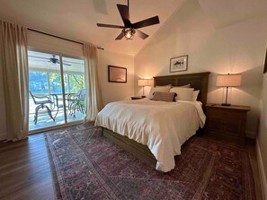 A bedroom with a bed, two bedside lamps, a ceiling fan, a large window with curtains, and a view of the outdoors. - Warluskee Luxury Lakefront Cottage w/ Hot Tub

 (Waleska)