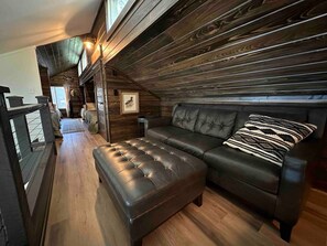 A cozy room with a wooden ceiling, a black leather sofa, and a matching ottoman. - Warluskee Luxury Lakefront Cottage w/ Hot Tub

 (Waleska)