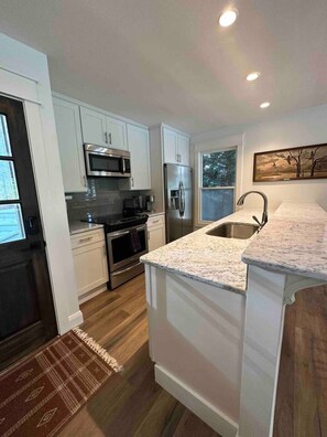 A modern kitchen with white cabinetry, stainless steel appliances, and a marble countertop.