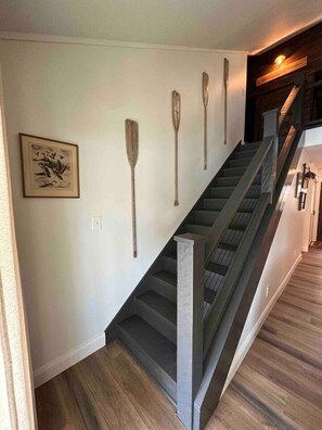 A staircase with a wooden finish and a handrail, leading to a landing with a framed artwork. - Warluskee Luxury Lakefront Cottage w/ Hot Tub

 (Waleska)
