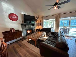 Una sala de estar acogedora con chimenea, un sofá de cuero, una mesa de centro de madera y un ventanal con vistas a un cuerpo de agua.