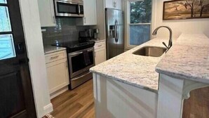 A modern kitchen with white cabinetry, stainless steel appliances, and a granite countertop. - Warluskee Luxury Lakefront Cottage w/ Hot Tub

 (Waleska)