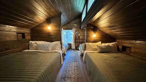 A cozy attic bedroom with two beds, a patterned rug, and wooden walls. - Warluskee Luxury Lakefront Cottage w/ Hot Tub

 (Waleska)