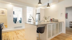 Une cuisine moderne dotée d’un îlot central, de luminaires suspendus et donnant sur l’espace de vie adjacent.