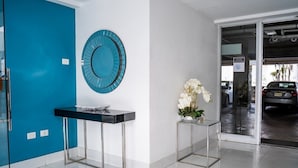 Ein moderner Empfangsbereich mit blauer Tür, einem Glastischchen und einem blauen Dekospiegel, dazu eine Vase mit weißen Blumen.