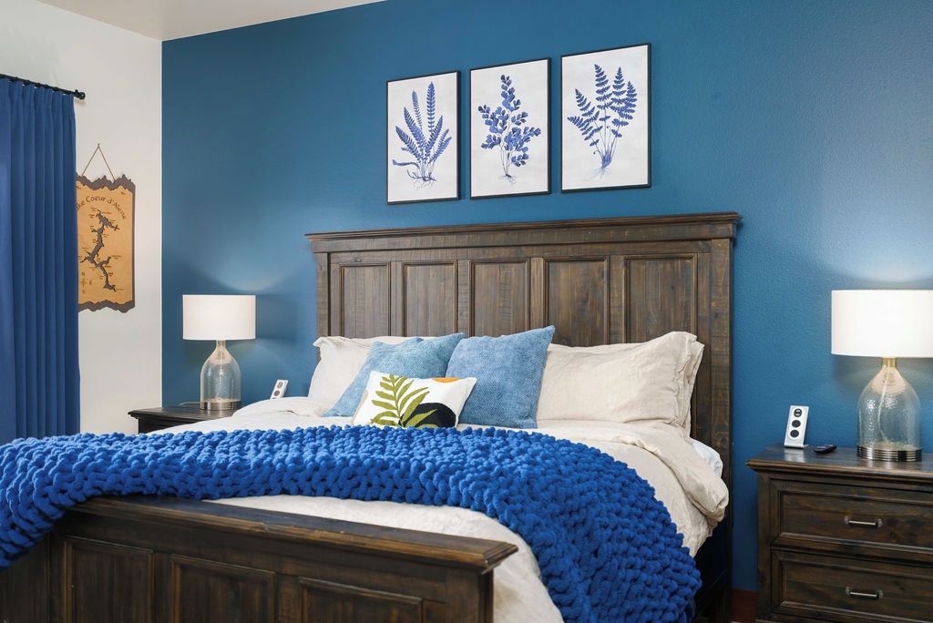 A bedroom with a dark wooden bed, blue bedding, and three framed botanical prints on the wall.