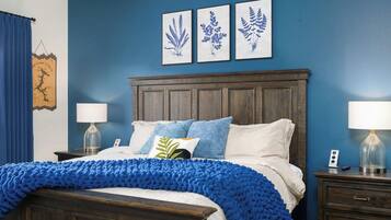 A bedroom with a dark wooden bed, blue bedding, and three framed botanical prints on the wall.