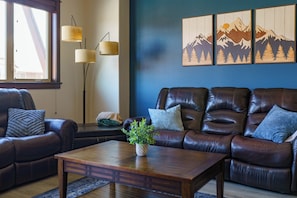 Ein Wohnzimmer mit einem braunen Ledersofa, einem Couchtisch aus Holz mit einer Pflanze und einer blauen Wand mit Berglandschaftsbildern.
