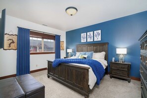 A bedroom with a bed, a nightstand, a dresser, a window with curtains, and wall art.
