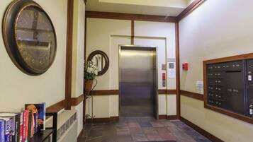 A hotel lobby with a reception desk, a clock, an elevator, and a mail slot.