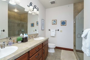 A bathroom with two sinks, a toilet, a large mirror, and a shower area.