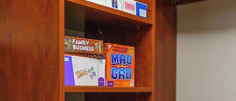 Ein Holzregal mit verschiedenen Gesellschaftsspielen, darunter 'Ticket to Ride', 'Mad Gab' und 'Scattergories'.