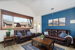 A living room with two leather sofas, a coffee table, a floor lamp, and a large window with a view of buildings. - Stylish, fully equipped 2-bed / 2-bath condo in Riverstone Village (Coeur d'Alene)