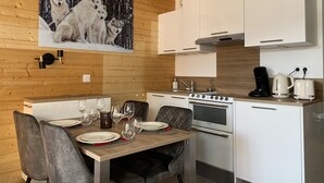 Una cocina moderna con armarios blancos, una estufa de acero inoxidable y una zona de comedor con mesa y sillas de madera.
