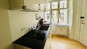 Una cocina con estufa negra, gabinetes blancos y una ventana con toallas de cocina colgadas.