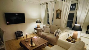 Una sala de estar con un sofá, una mesa de centro, un televisor y una lámpara.