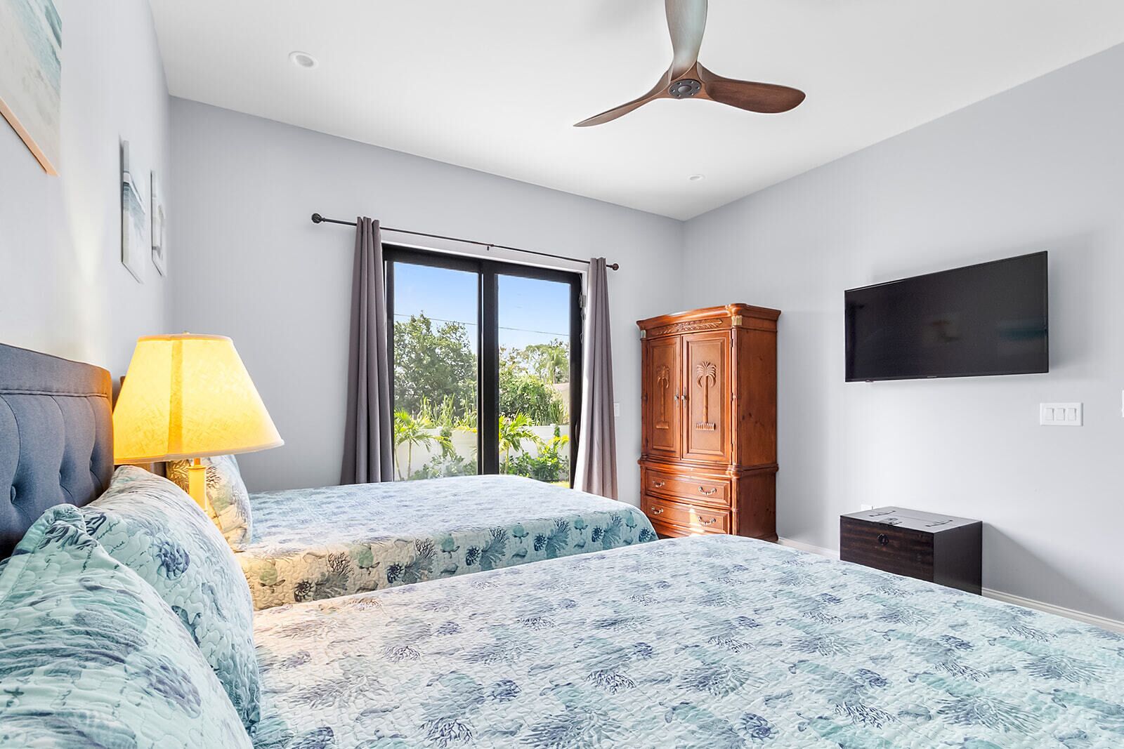 A bedroom with two beds, a ceiling fan, a TV, and a wardrobe.