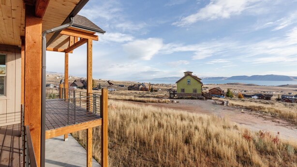 Une terrasse en bois offrant une vue sur une maison verdoyante et des montagnes lointaines.