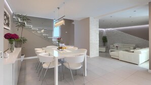 A modern living room with a white sofa, a dining area with a white table and chairs, and a staircase with a white brick wall. - Amazing home in Porec (Porec)