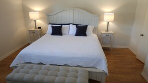 A neatly made bed with a white and navy blue bedspread, flanked by two bedside tables with lamps, a bench at the foot of the bed, and a wooden floor. - Casey Key/Nokomis Florida home, minutes to the beach (Nokomis)