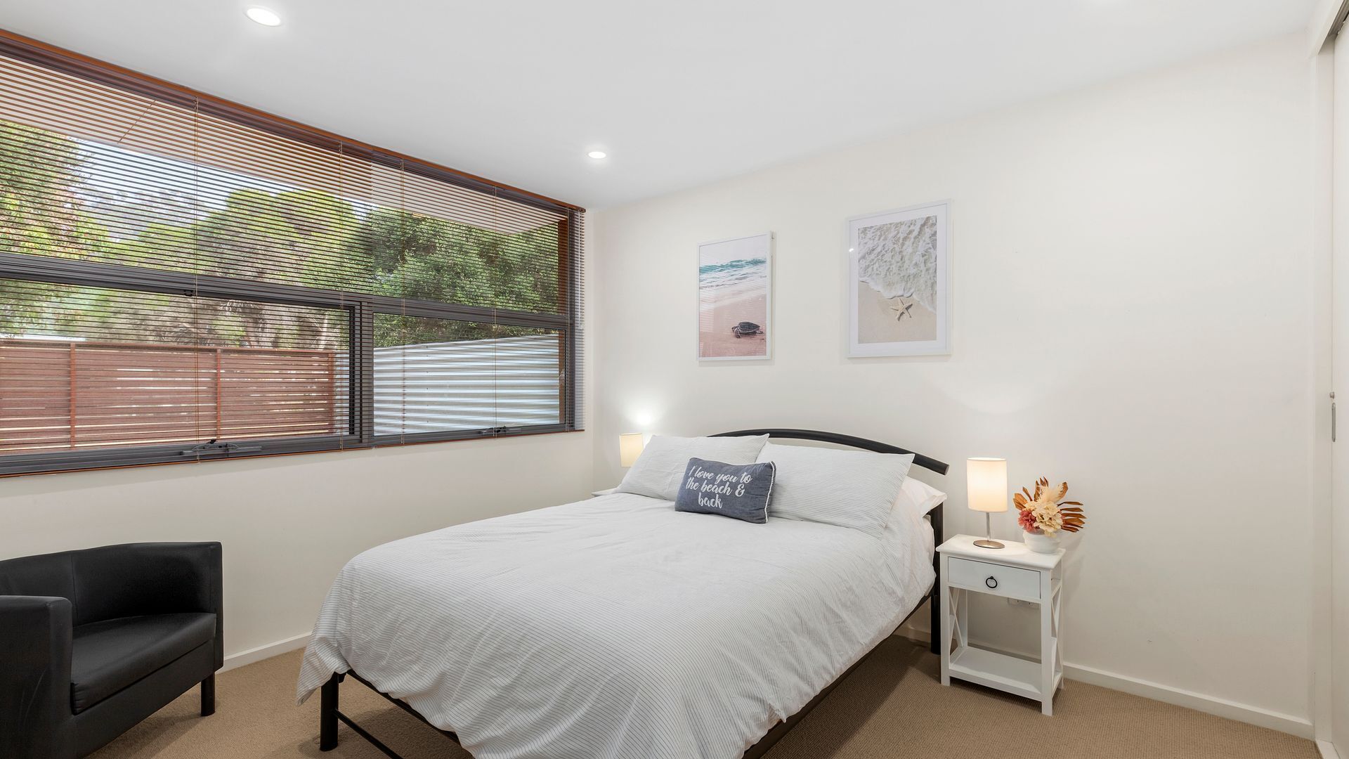 A bedroom with a bed, a nightstand, a chair, and a window with blinds.