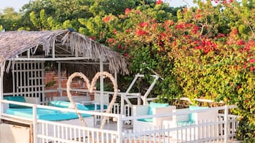 A thatched-roof structure with a white fence, a pool, and blue cushions.