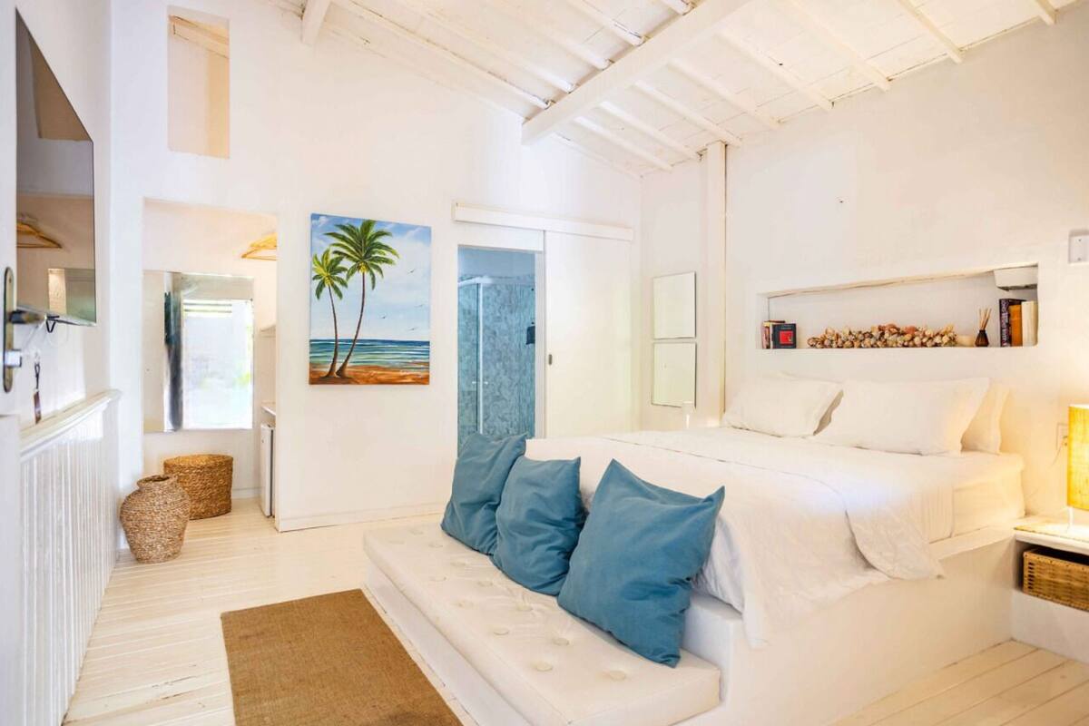 Ein heller, weißer Raum mit einem Bett, einem Schlafsofa und einem Gemälde mit einer Strandansicht.