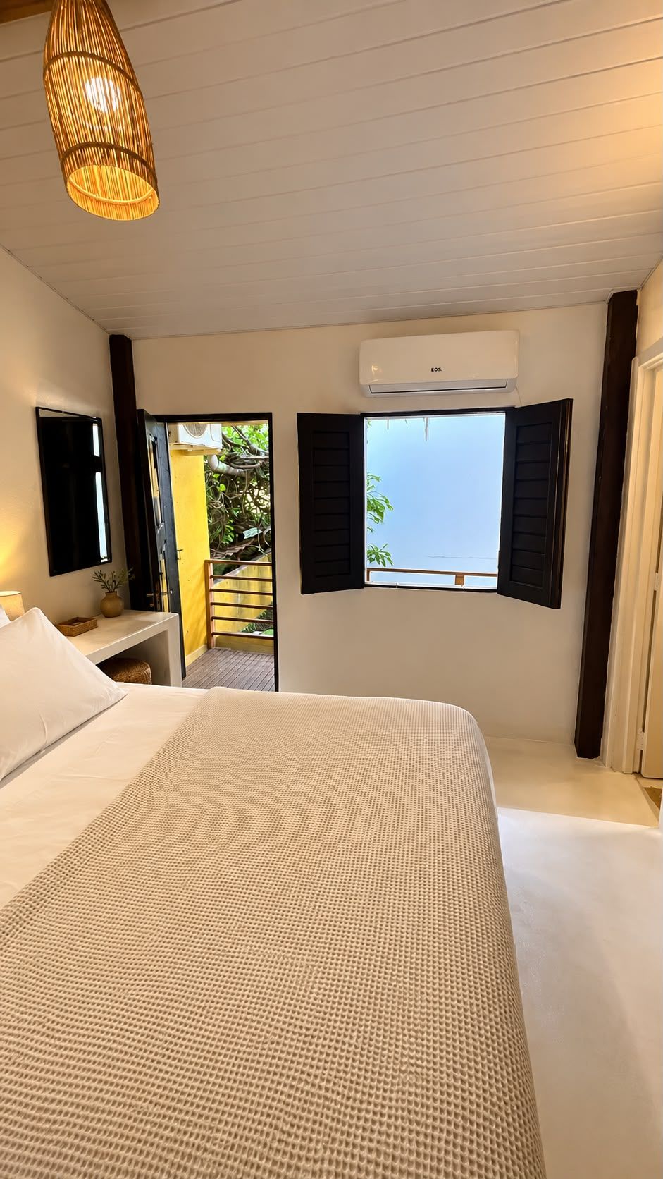 Une chambre d’hôtel équipée d’un lit, d’une table de chevet, d’un appareil de climatisation et d’une fenêtre avec des volets.