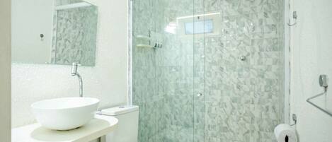 Un baño con lavamanos blanco, inodoro y ducha con mampara de vidrio.
