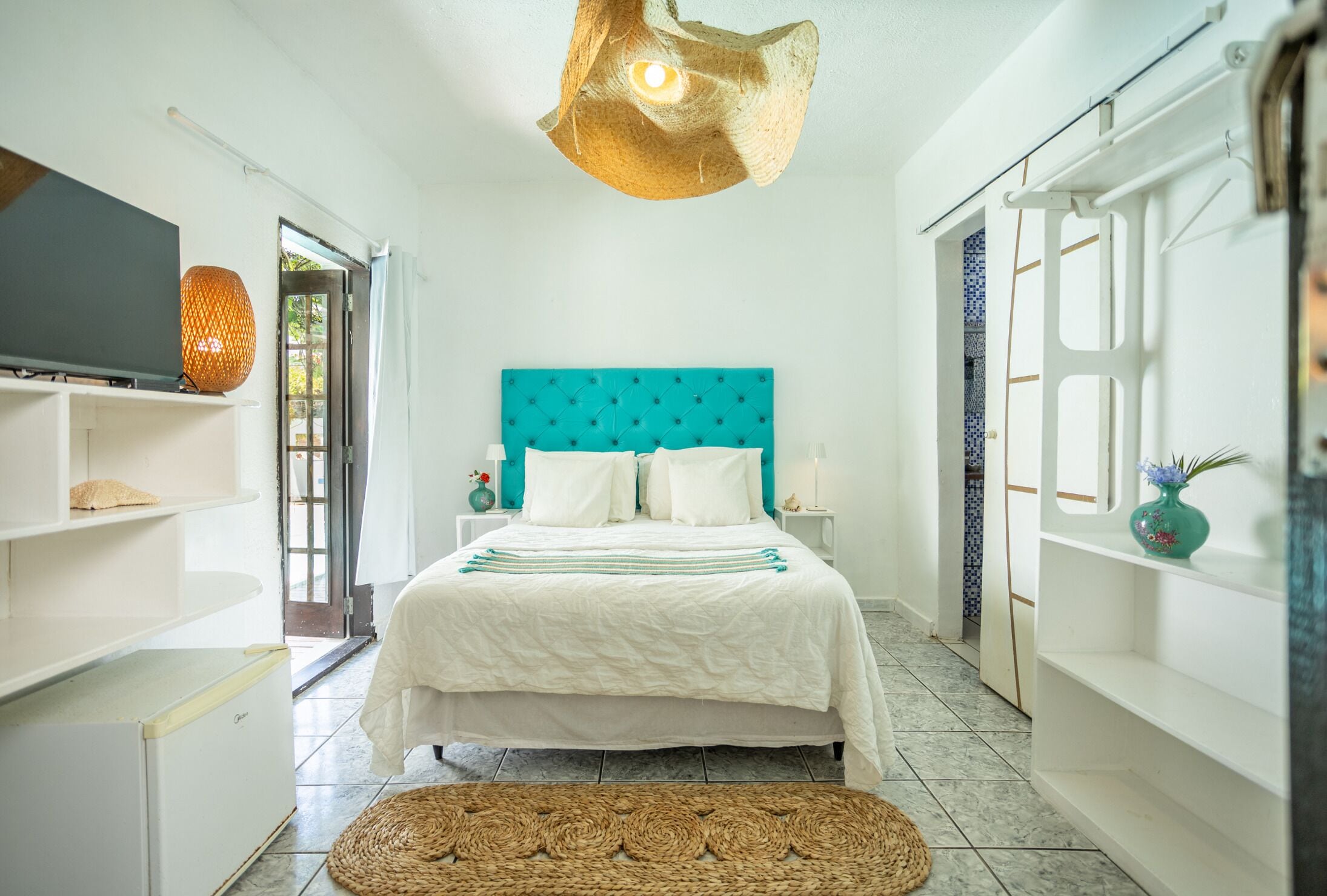 A bedroom with a bed, a television, a unique light fixture, and a view of the outdoors.